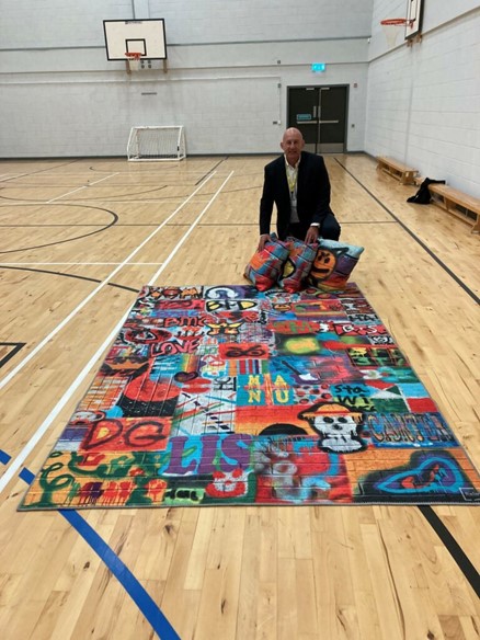 A man in a school gym hall with a large rug and cushions