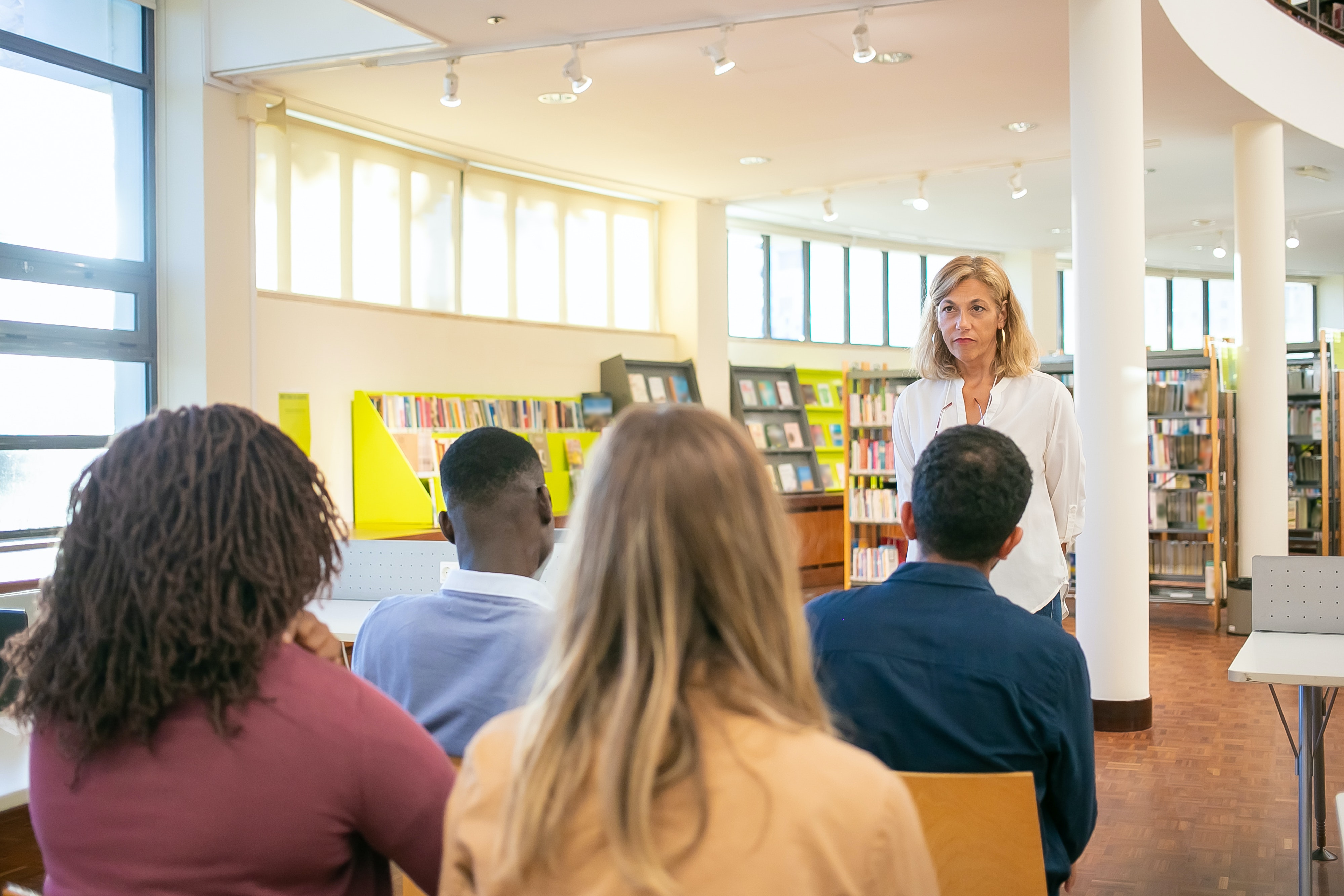 A number of people sat in a library listening to a woman talk at the front of the room