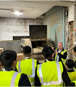 A group of young people in high vis listening to a man speak