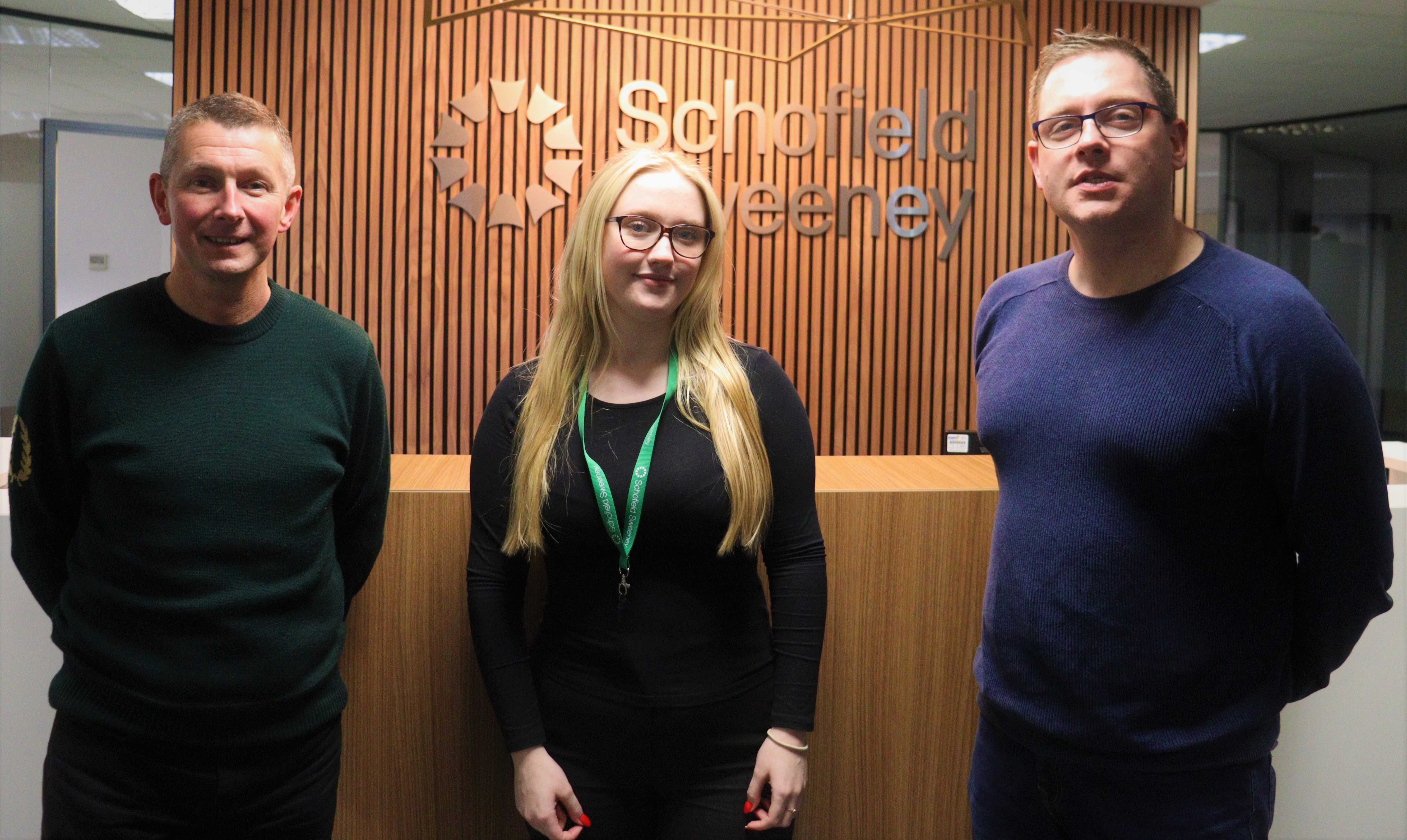 Two men and a young woman stood in front of Schofield Sweeney reception desk