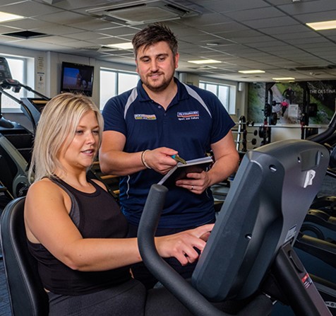 A man in uniform talking to a woman on fitness equipment