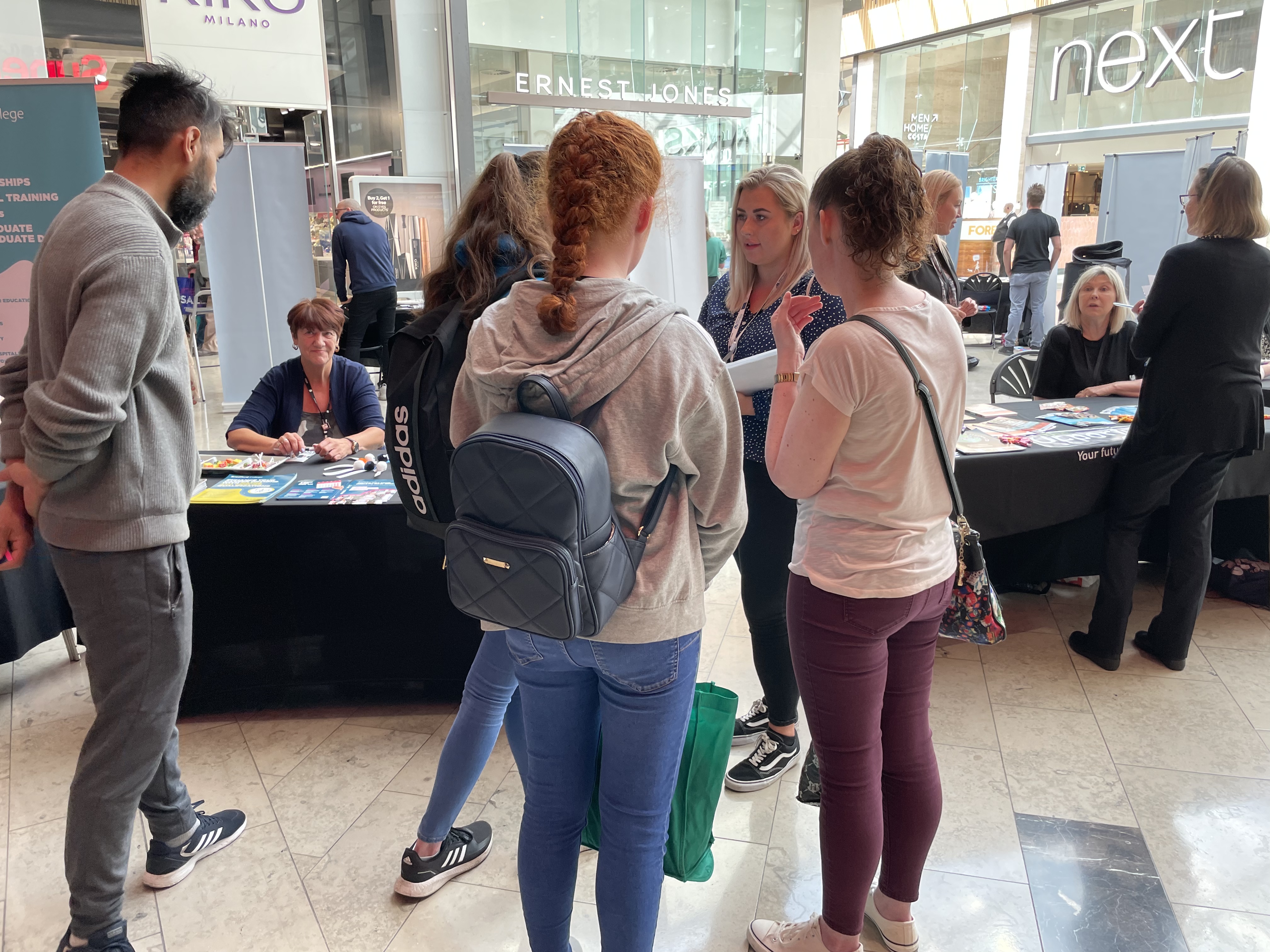 A group of young women talking to a woman wearing an ID badge in front of a stall