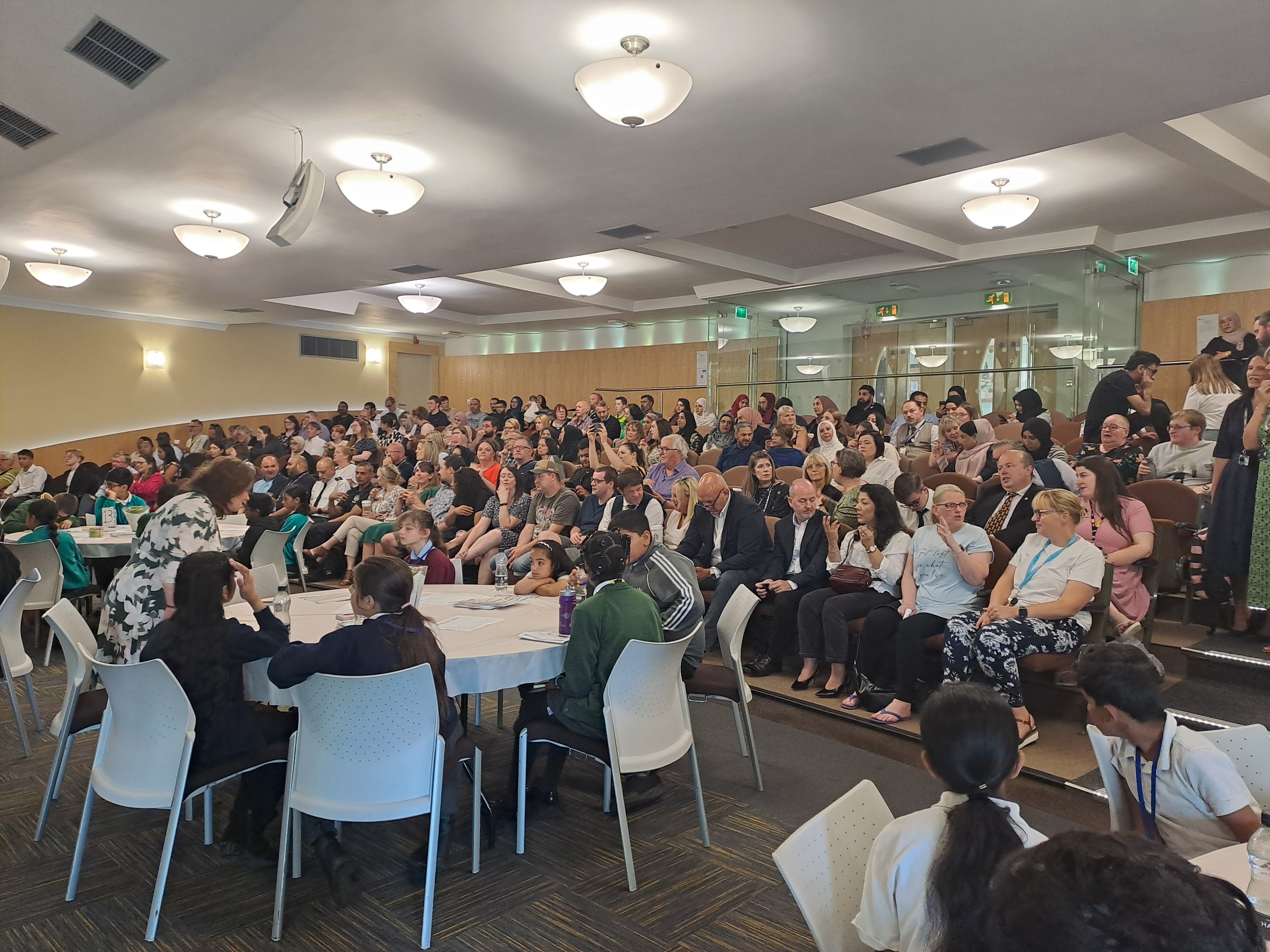 A room with young people at tables and adults sat in rows