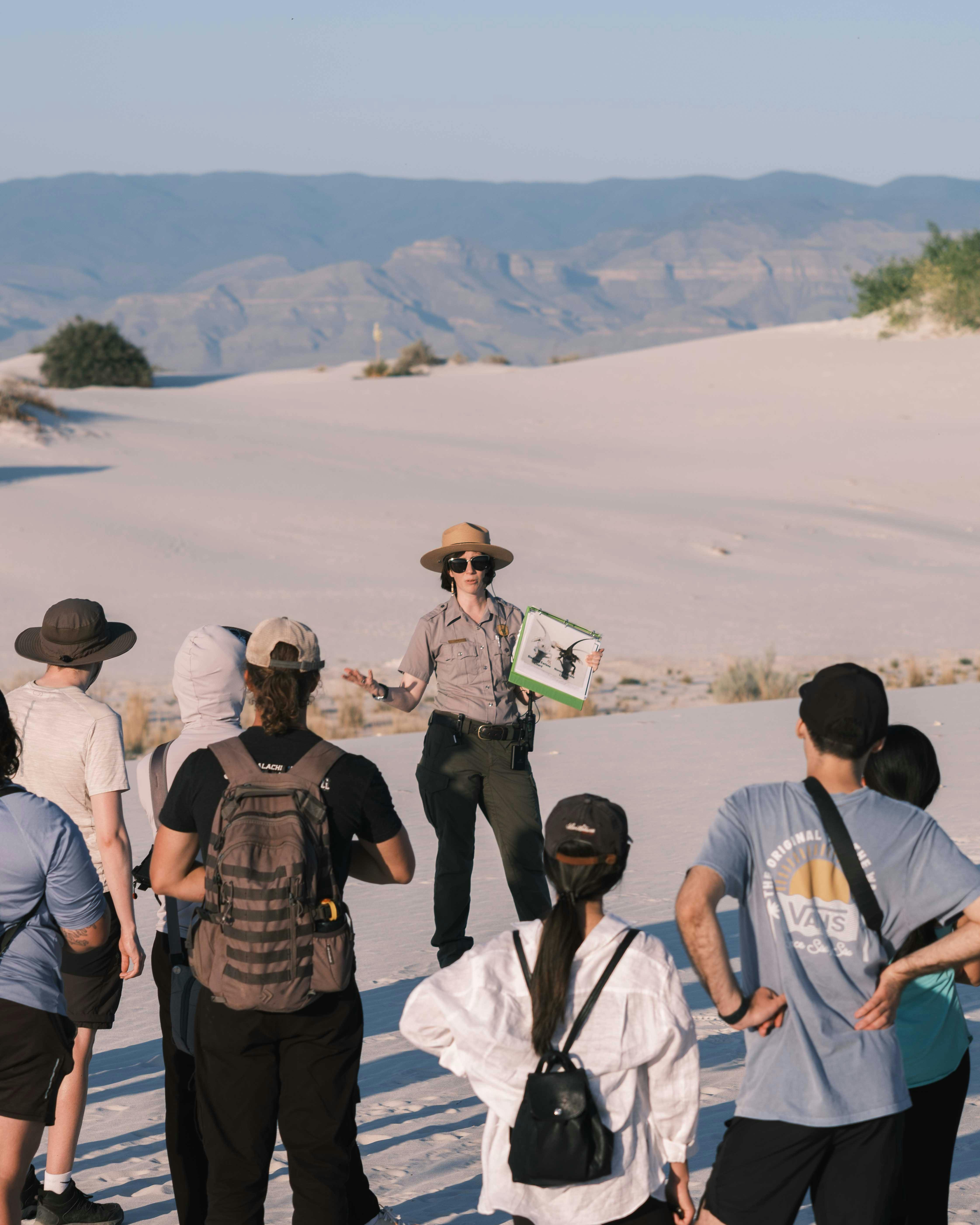 A woman in uniform in front of a group of people in a desert
