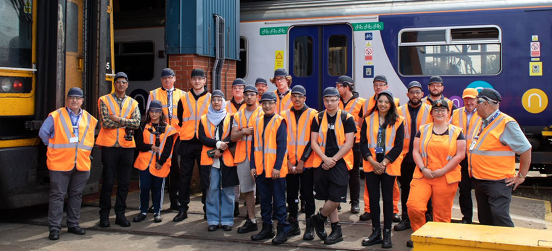 A group photo of lots of young people wearing high vis in front of a train
