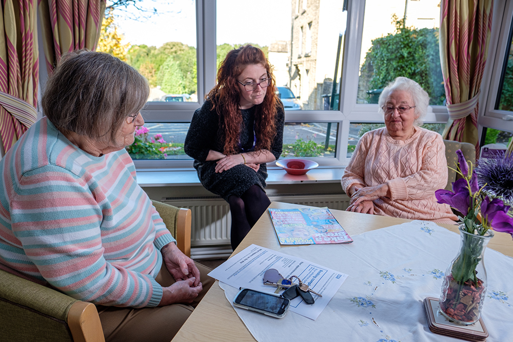 Two older women sat at a table discussing paperwork with a younger woman
