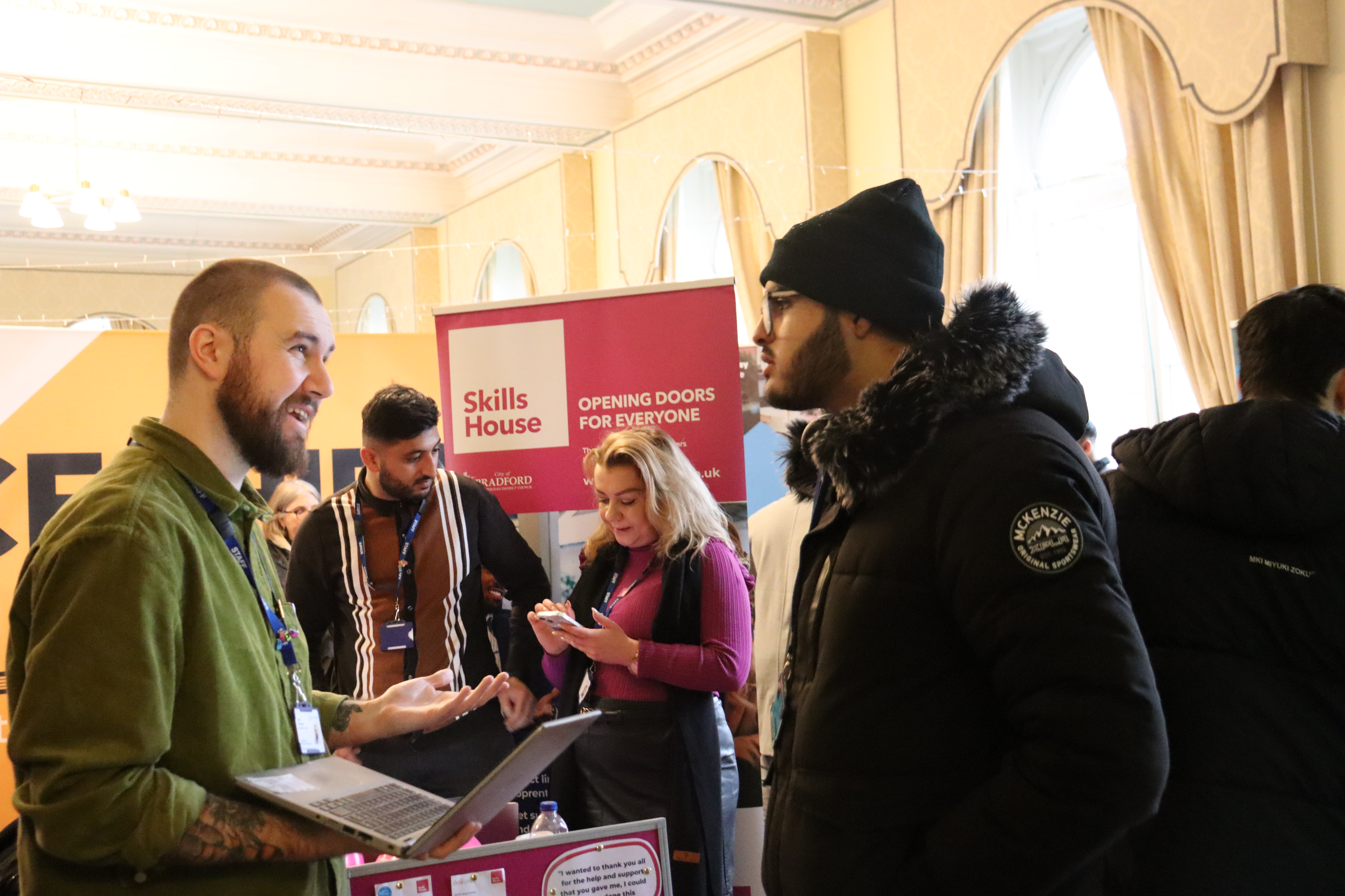 A man talking to a young man in front of a SkillsHouse banner