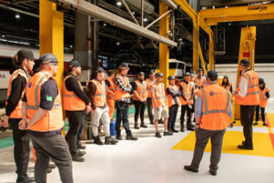 A man talking to a group of young people, all of them wearing high vis