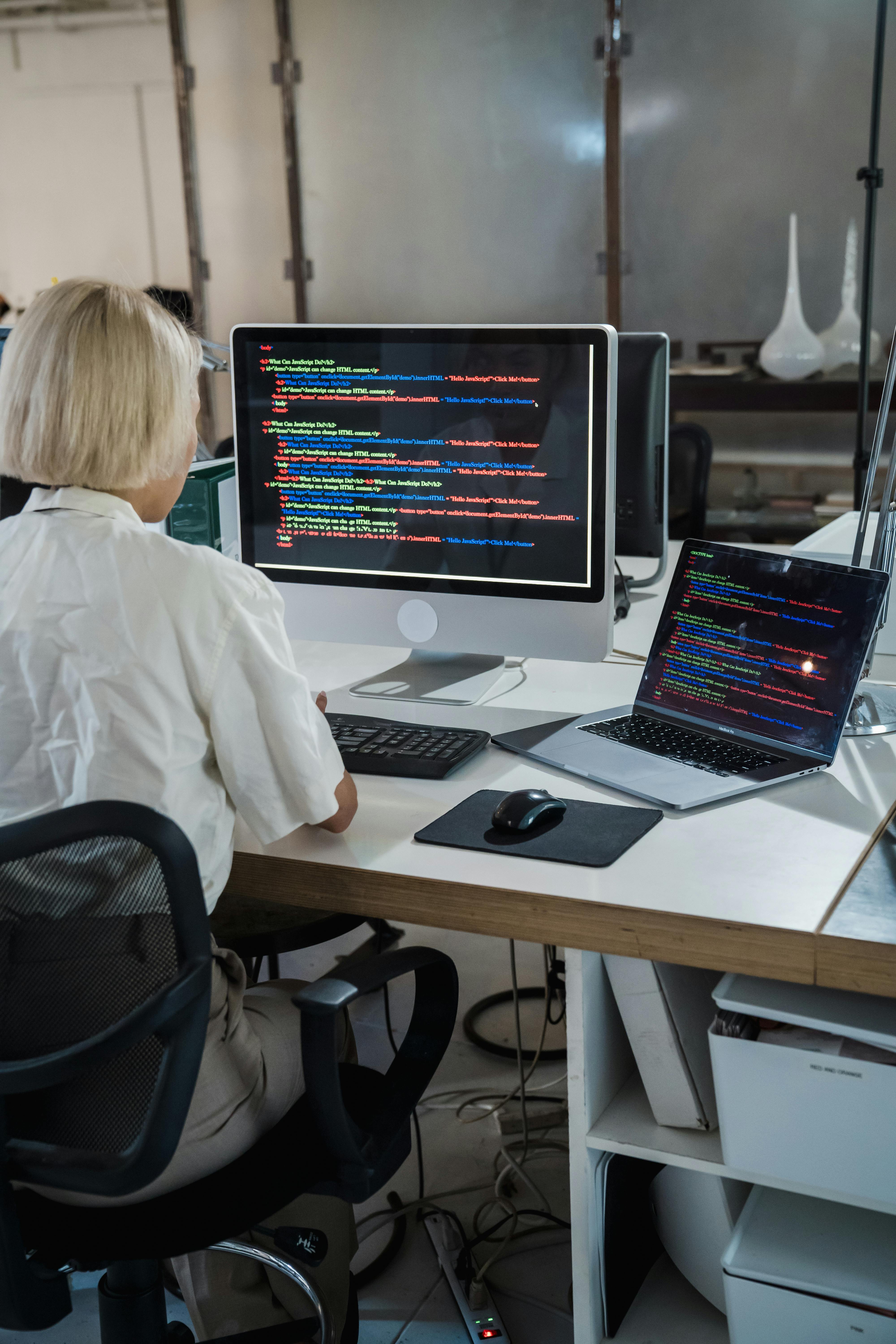 The back of a woman working on two computer screens which are covered in code language