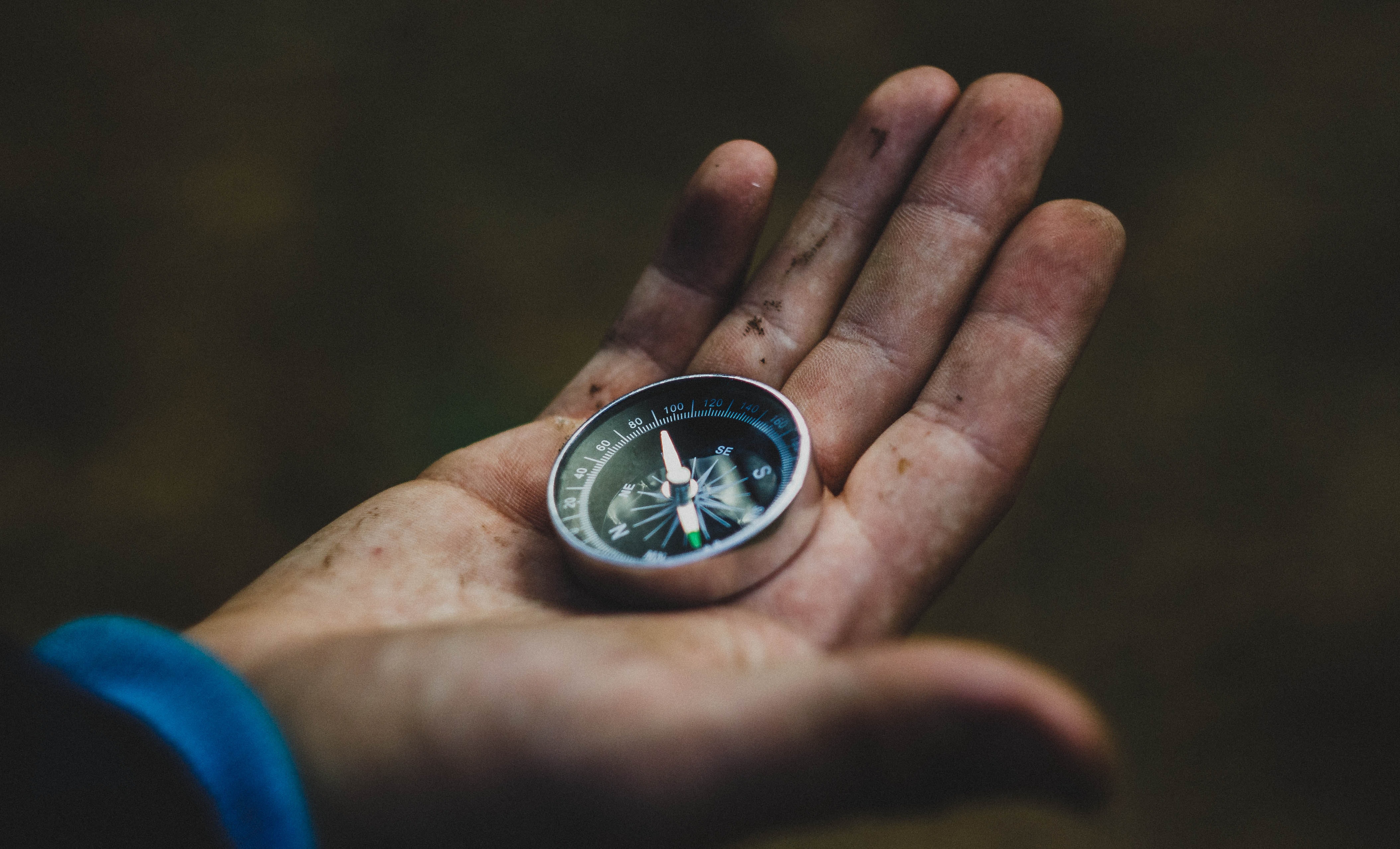A muddy hand holding a compass