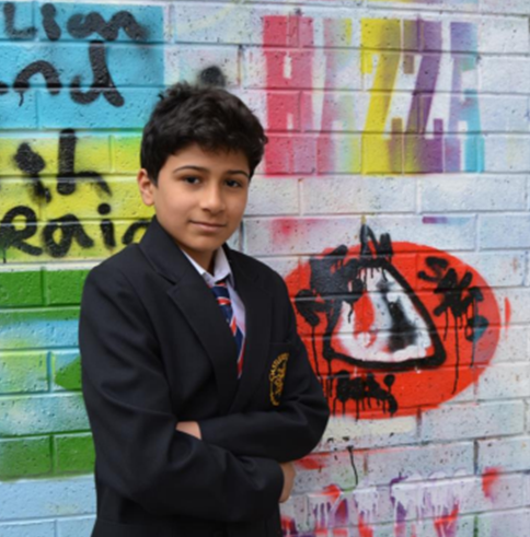 A young boy stood in front of a graffitied wall