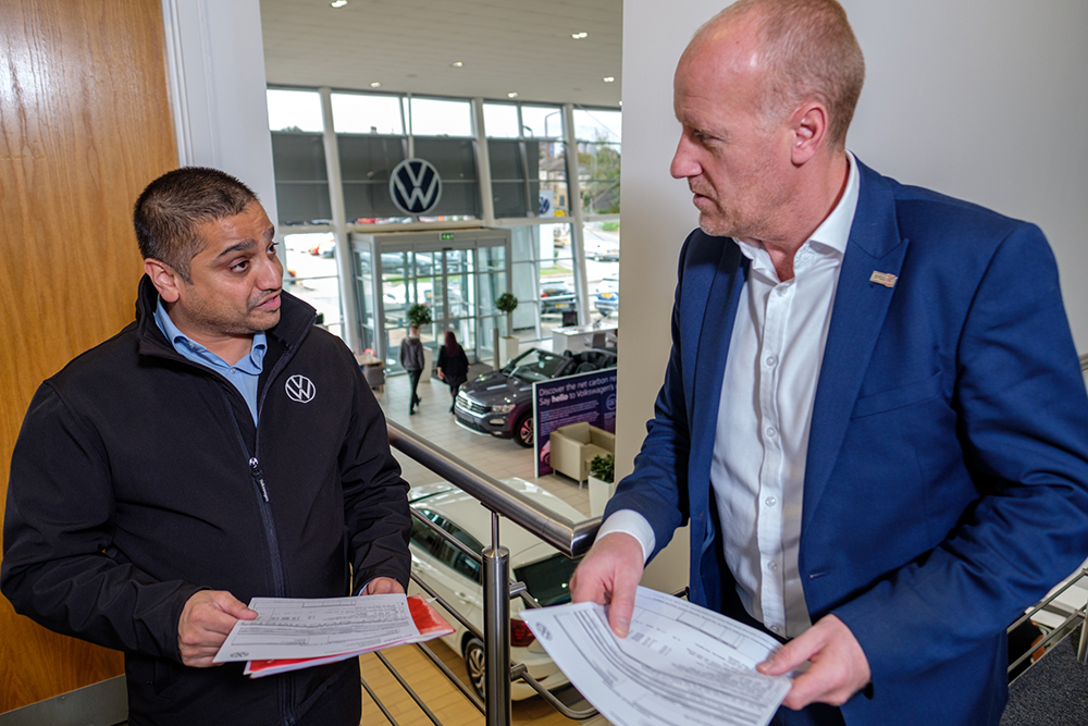 Two men in a car showroom discussing paperwork