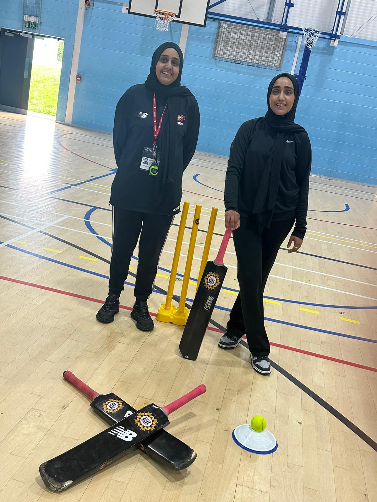 Two girls in a sports hall using cricket equipment