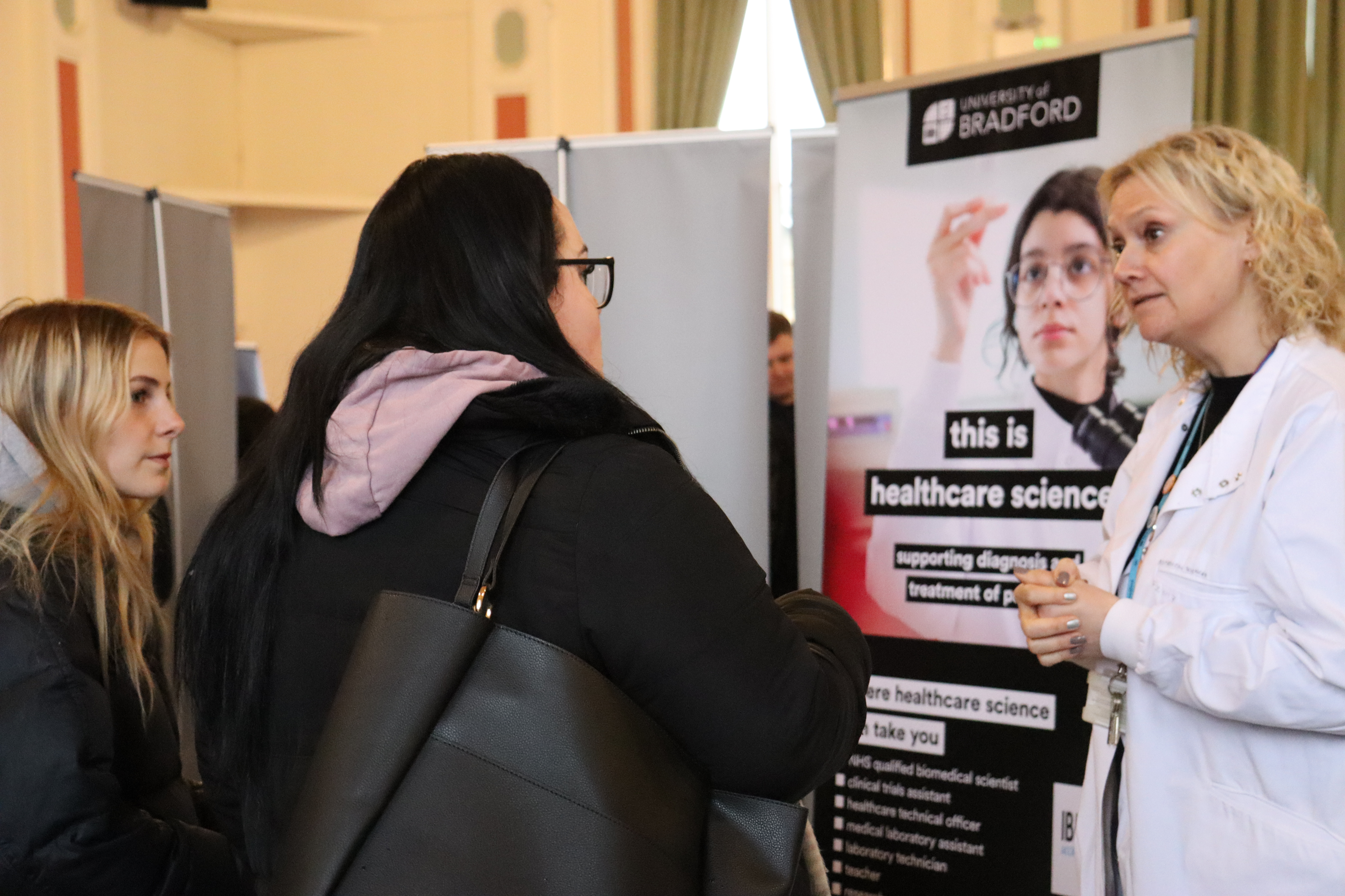 A woman in a white lab coat talking to young people