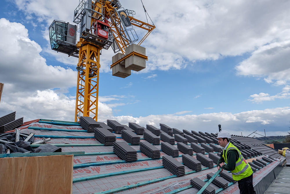 A man in hi vis jacket and hard hat on a roof with piles of roof tiles around