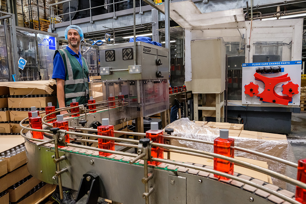 A man wearing a hairnet and hi vis jacket stood next to a factory production line