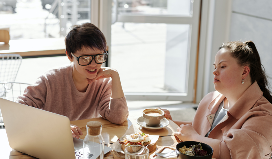 A young woman with Down syndrome sat with an older woman in a cafe
