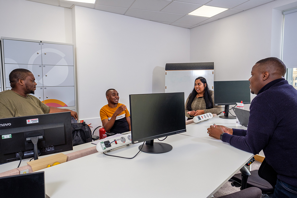 Four people sat around a desk in front of computers
