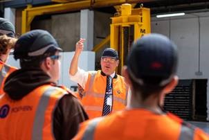 A man talking to a group of young people, all of them wearing high vis
