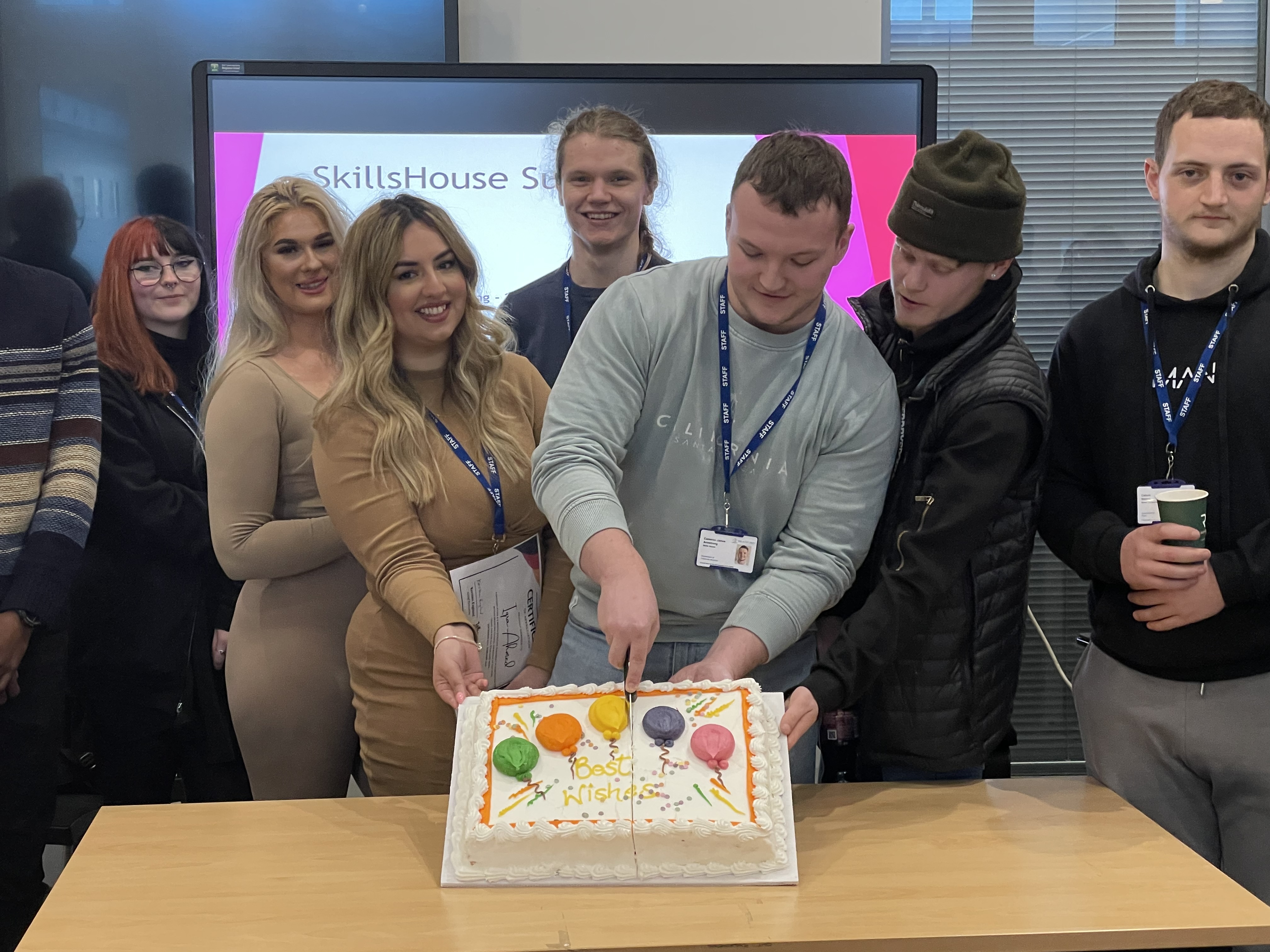 A group of Kickstarters cutting a cake that reads best wishes