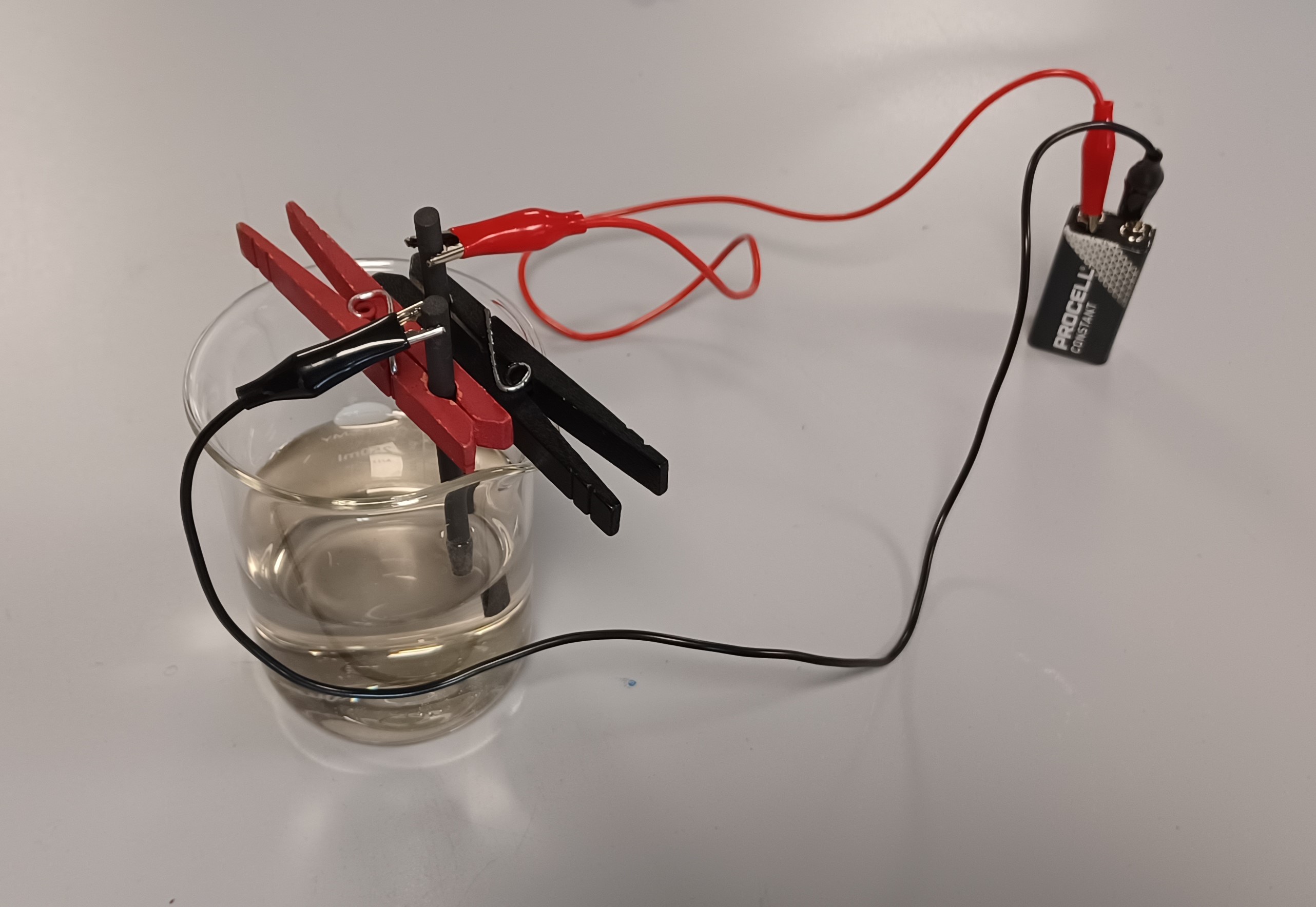 A glass of water with clips and wires leading to a battery